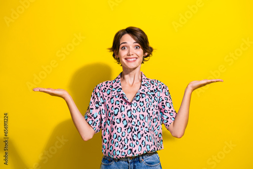 Portrait of cheerful nice lady beaming smile arms palms hold empty space vs scales isolated on yellow color background