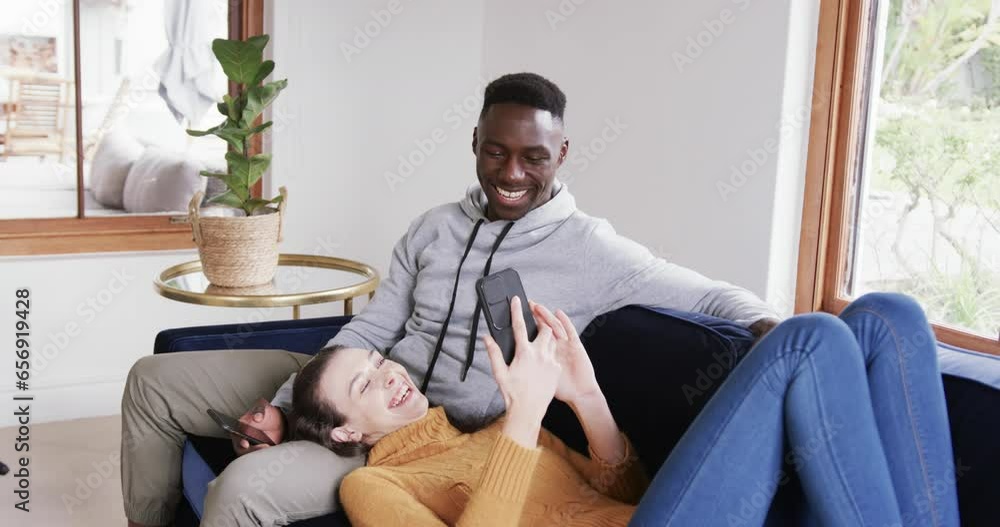 Happy diverse couple sitting and lying on sofa and using smartphones in home,copy space Happy diverse couple sitting and lying on sofa and using smartphones in home,copy space