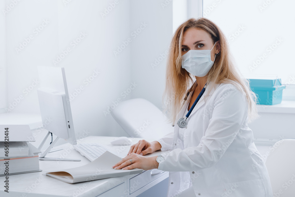 Portrait of a doctor woman in a protective mask at her workplace in the office. The doctor looks at the camera. Portrait of a doctor woman in a protective mask at her workplace in the office. The doctor looks at the camera.