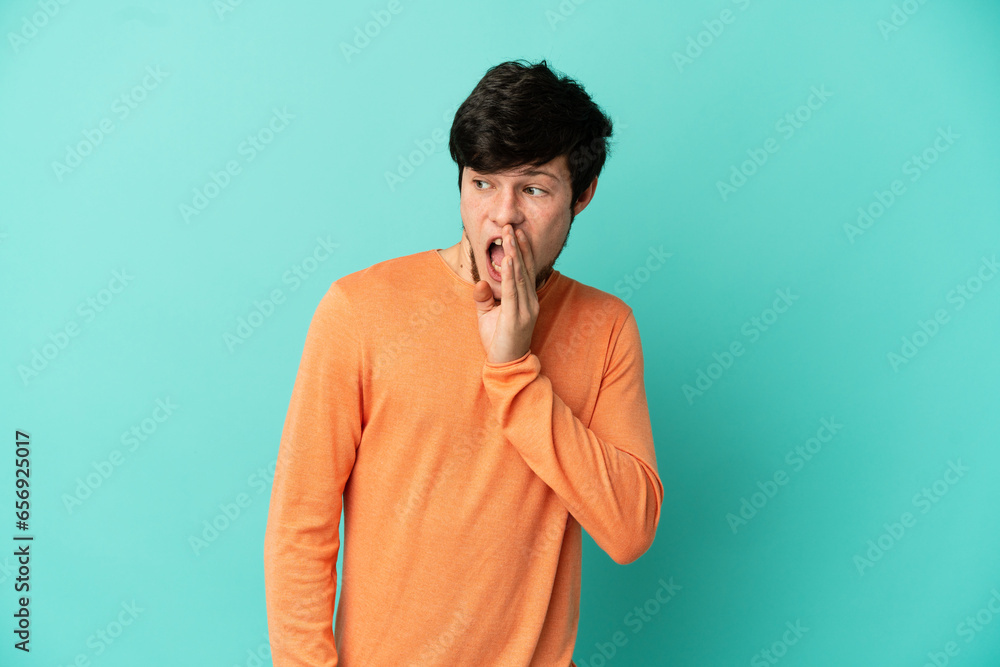 Young Russian man isolated on blue background whispering something with surprise gesture while looking to the side Young Russian man isolated on blue background whispering something with surprise gesture while looking to the side