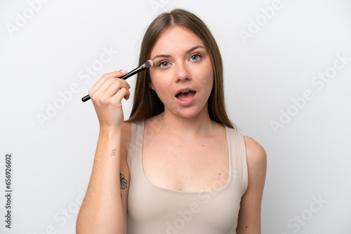 Young Lithuanian woman isolated on white background holding makeup brush and surprised