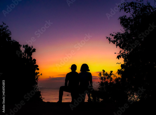 silhouette of a couple sitting on a bench at sunset photo