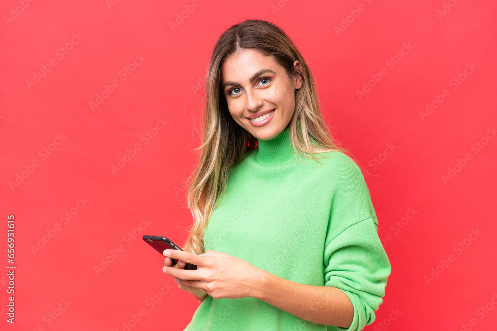 Young Uruguayan woman isolated on red background sending a message with the mobile Young Uruguayan woman isolated on red background sending a message with the mobile