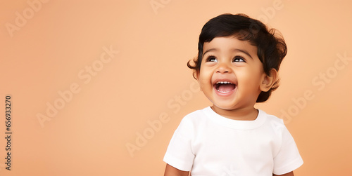 Adorable Indian toddler laughing wearing white shirt, isolated on pastel orange background © Jamo Images