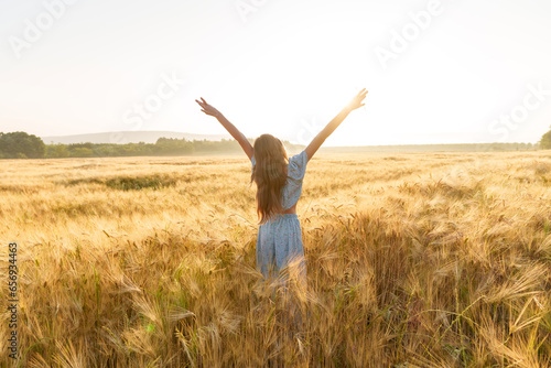 Girl with long hair stretching arms amidst wheat crop in field photo