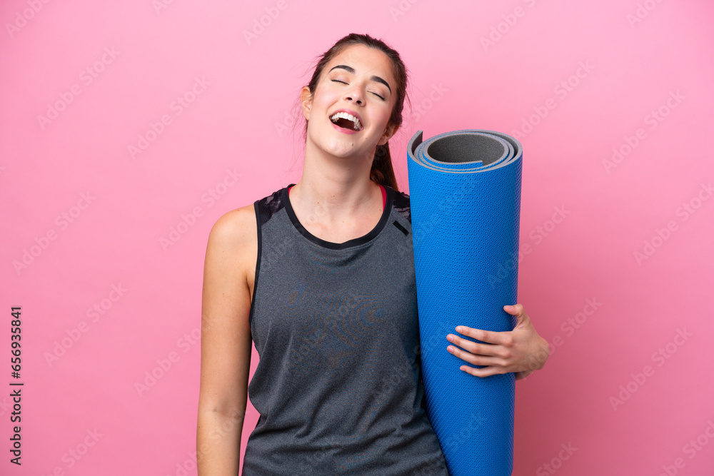 Young Brazilian sport woman going to yoga classes while holding a mat isolated on pink background laughing Young Brazilian sport woman going to yoga classes while holding a mat isolated on pink background laughing