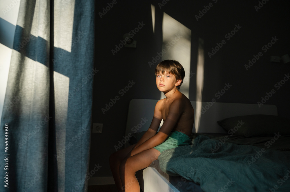 Thoughtful boy sitting on bed at home Thoughtful boy sitting on bed at home