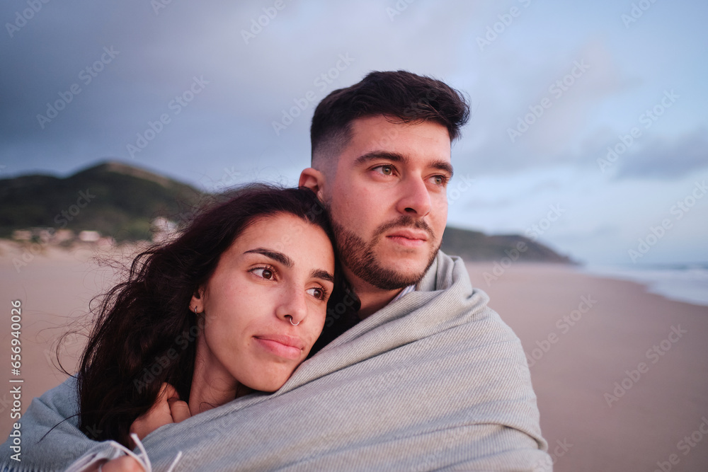 Contemplative couple covered in blanket at beach Contemplative couple covered in blanket at beach