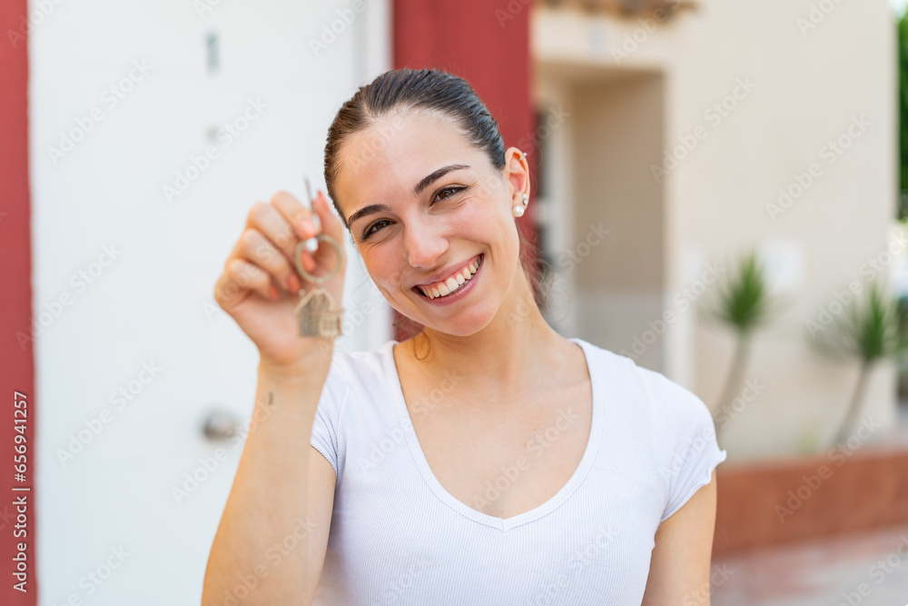 Young pretty woman at outdoors holding home keys with happy expression Young pretty woman at outdoors holding home keys with happy expression