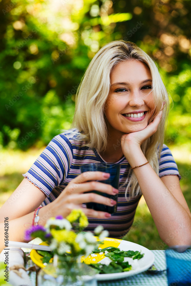Happy blond woman sitting at picnic table in garden Happy blond woman sitting at picnic table in garden