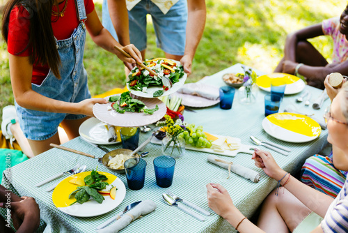 Friends serving food at picnic table in garden