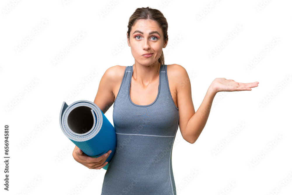 Pretty Young Uruguayan sport woman going to yoga classes while holding a mat over isolated background having doubts while raising hands Pretty Young Uruguayan sport woman going to yoga classes while holding a mat over isolated background having doubts while raising hands