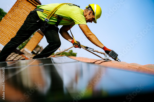 Engineer wearing hardhat using drill machine to install solar panel on roof photo