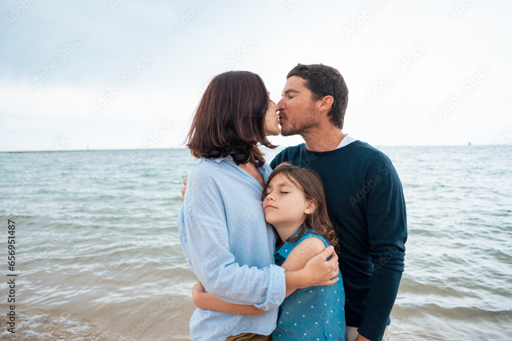 Father and mother kissing each other with daughter in front of sea Father and mother kissing each other with daughter in front of sea