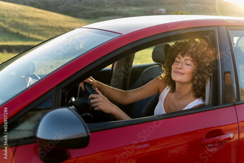 Smiling woman with eyes closed driving red car