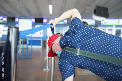 Man in a protective mask raises access tape and goes to registration without queue. Violation of rules of medical and passport control in public places airport station