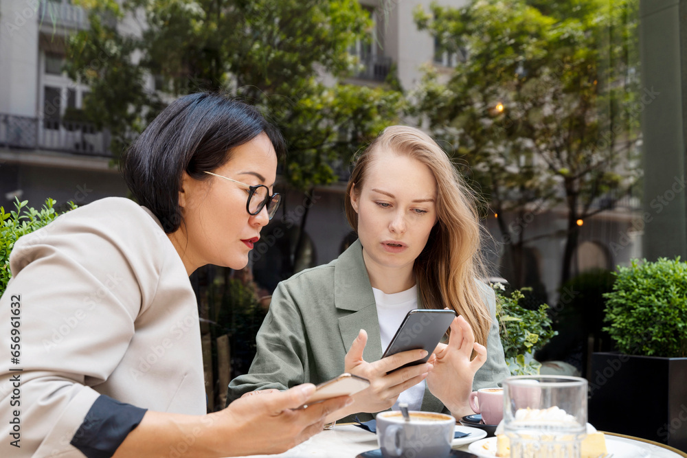 Businesswoman showing over smart phone to partner sitting at sidewalk cafe Businesswoman showing over smart phone to partner sitting at sidewalk cafe