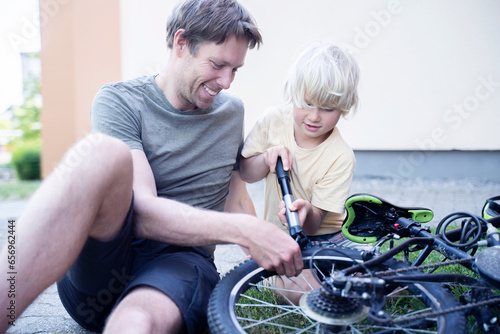 Happy father and son with pump repairing bicycle at footpath