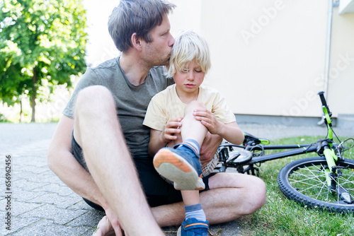Father kissing and caring son fallen down from bicycle at footpath