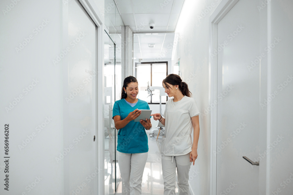Happy dentist discussing with colleague over tablet PC in corridor Happy dentist discussing with colleague over tablet PC in corridor