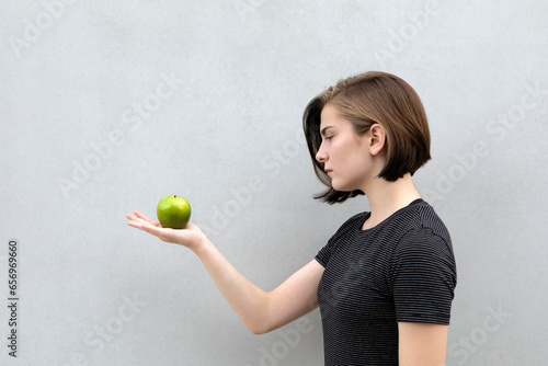 Teenage girl holding green apple against gray background photo