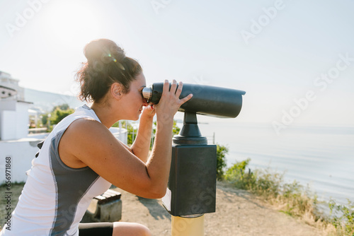 Woman looking through stationary binoculars on sunny day photo