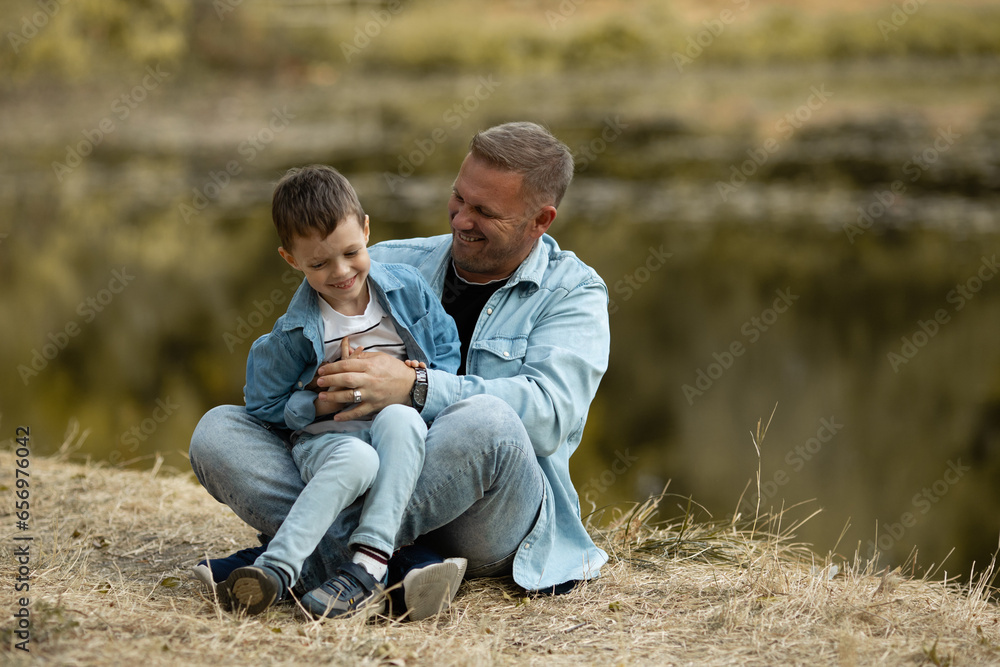 Dad and son have fun on the shore of the lake in the forest. Happy family with child kid boy playing and having fun outdoors over autumn park background. Dad and son have fun on the shore of the lake in the forest. Happy family with child kid boy playing and having fun outdoors over autumn park background.