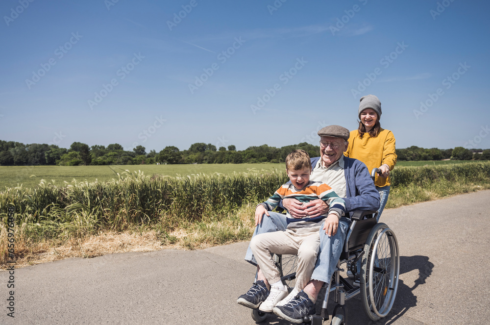 Girl with grandfather and grandson sitting in wheelchair on road Girl with grandfather and grandson sitting in wheelchair on road
