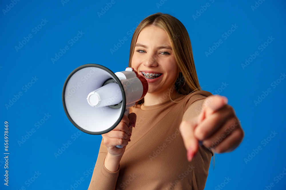 Teen girl making announcement with megaphone on blue background Teen girl making announcement with megaphone on blue background