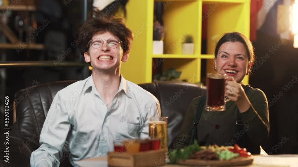 A young, smiling, beautiful couple watches a sports match, cheers, and celebrates a scored goal while sitting in a bar with beer A young, smiling, beautiful couple watches a sports match, cheers, and celebrates a scored goal while sitting in a bar with beer
