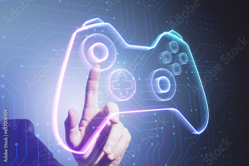 Close up of male hand pointing at creative joystick or gamepad hologram on blurry background. Esport, gaming and fun concept. photo