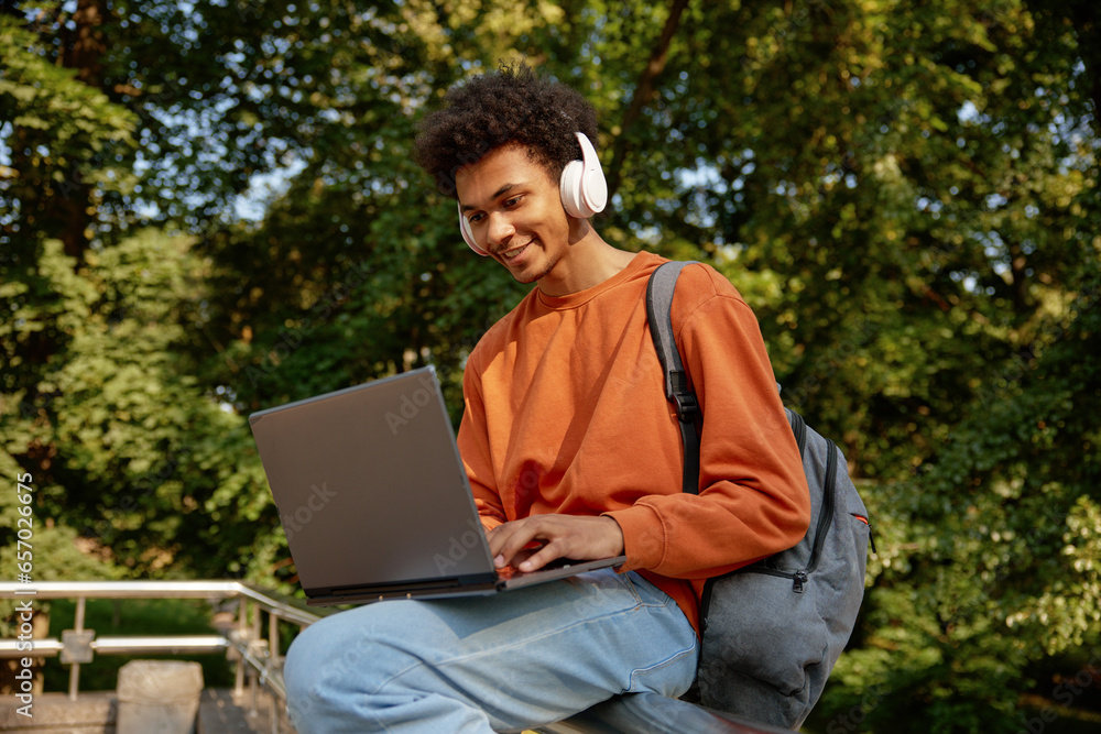 Happy smiling male student wearing wireless headphones using laptop