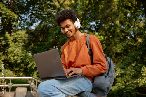 Obraz na płótnie Happy smiling male student wearing wireless headphones using laptop w salonie
