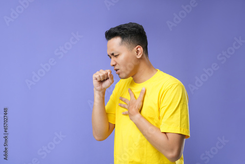 A young Asian man feeling a sore throat and flu symptoms  coughing with his mouth covered. Isolated on a purple background.