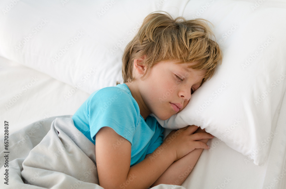 6-7 year old boy sleeping peacefully in bed on a white pillow in the morning. blond little kid in blue pajamas in a cozy bed with white bedding resting and dreaming very comfortably in bright bedroom 6-7 year old boy sleeping peacefully in bed on a white pillow in the morning. blond little kid in blue pajamas in a cozy bed with white bedding resting and dreaming very comfortably in bright bedroom