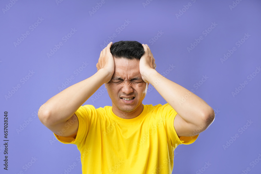 Photo of a young Asian man, suffering from headaches desperate and stressed because of pain and migraine. Hands on head. Photo of a young Asian man, suffering from headaches desperate and stressed because of pain and migraine. Hands on head.