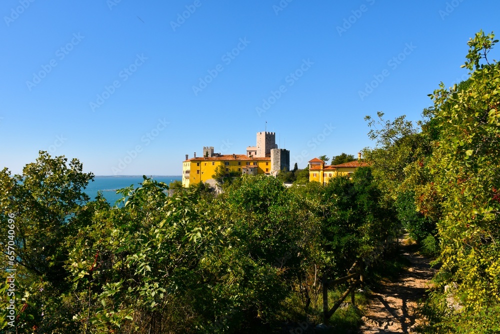 Trail leading through a mediterranean forest and Duino castle behind in Duino-Aurisina, Italy