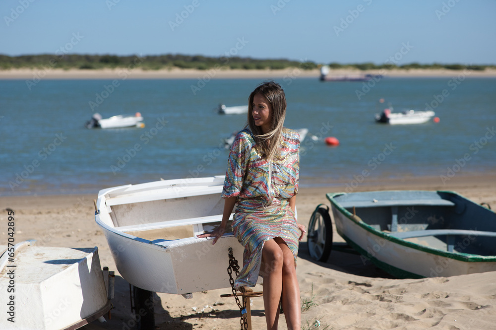 Pretty young blonde woman sitting in the fishermen's boats on the seashore. In the background on the horizon the blue sea and the biosphere reserve of the natural park and the mouth of the river