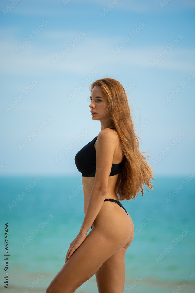 Beautiful young woman in black bikini on the beach at sunset.