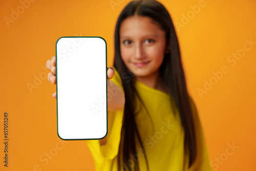 Teen girl showing smartphone screen with copy space over yellow background