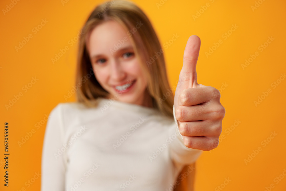 Teen girl showing thumb up sign against yellow background Teen girl showing thumb up sign against yellow background