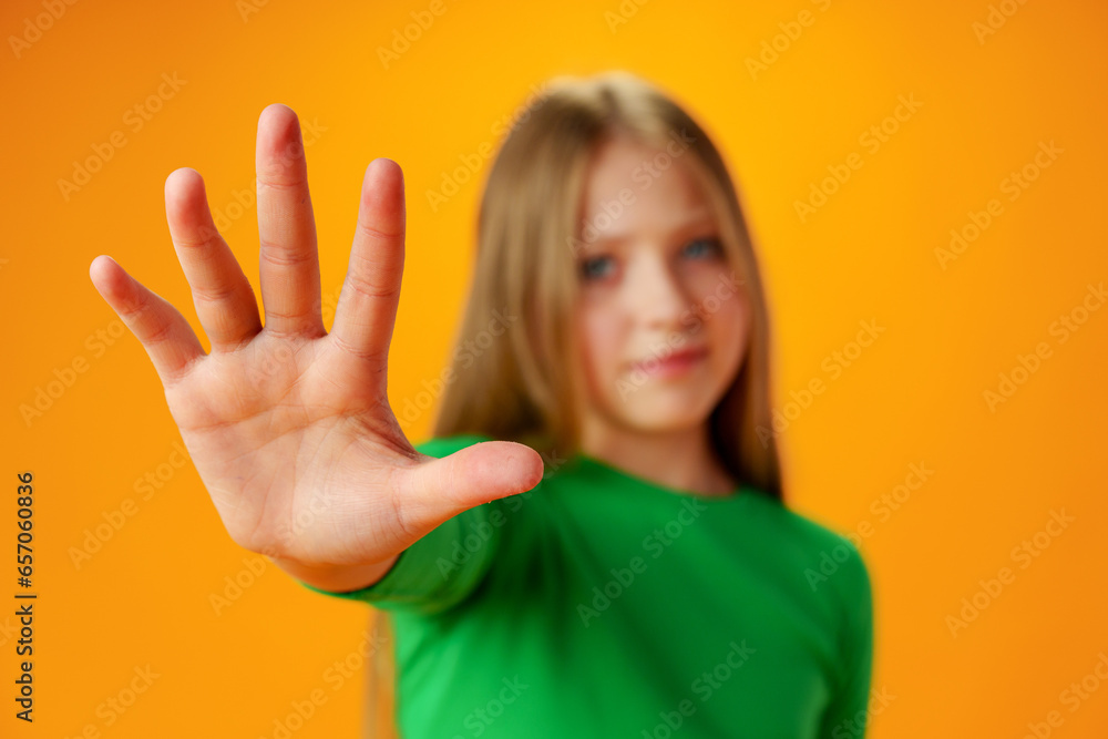 Teen girl extend hand in block gesture against yellow background Teen girl extend hand in block gesture against yellow background