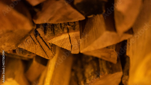Firewood heap of natural timber in semi-dark room closeup. Dry woodpile stack prepared for domestic fireplace burning at home. Chopped lamber stock for fireside in house at warm light