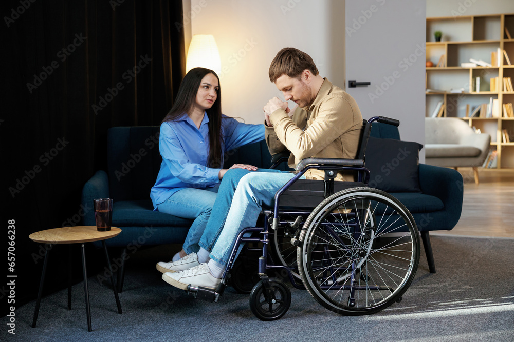 Young man in a wheelchair. Girlfriend comforting her sad boyfriend Young man in a wheelchair. Girlfriend comforting her sad boyfriend