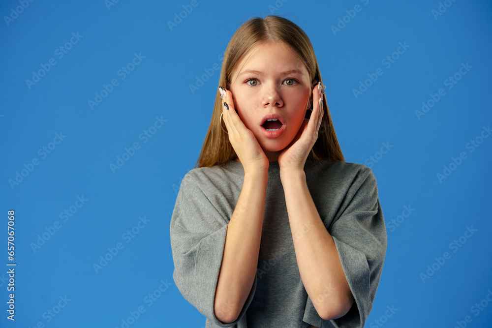 Wall Mural Surprised amazed teen girl against blue background in studio