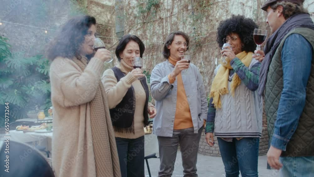 Group of cheerful friends standing outdoors in the backyard, clinking wine glasses in a toast, smiling and chatting while having barbecue party together on autumn day Group of cheerful friends standing outdoors in the backyard, clinking wine glasses in a toast, smiling and chatting while having barbecue party together on autumn day