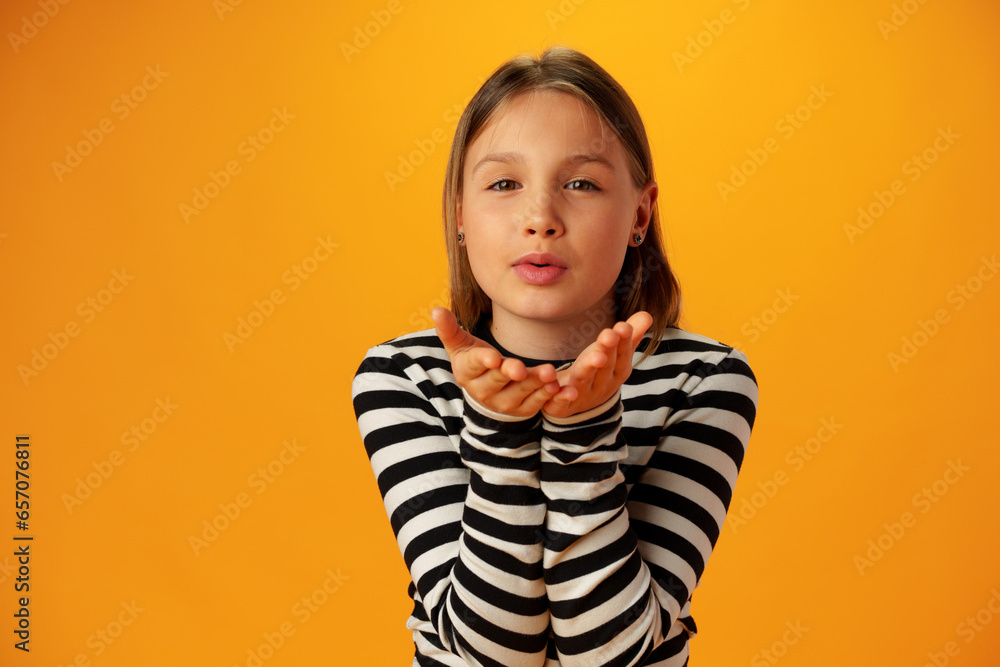 Teen girl blowing a kiss against yellow background in studio Teen girl blowing a kiss against yellow background in studio
