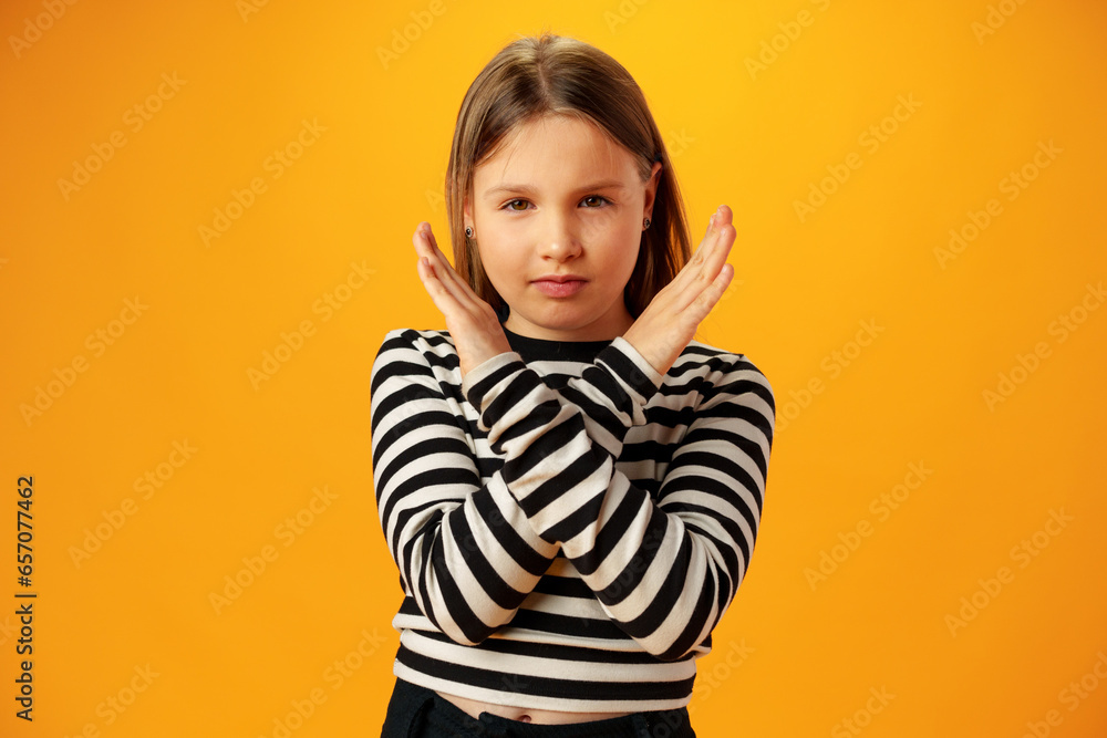 Teen girl shows cross hands gesture, rejecting something over yellow background in studio Teen girl shows cross hands gesture, rejecting something over yellow background in studio