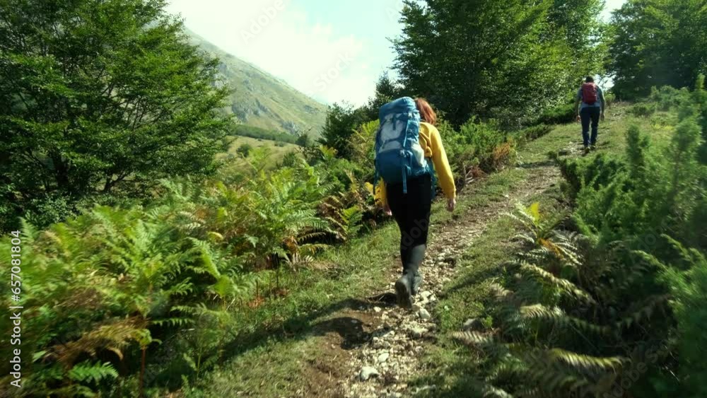 A guy and a girl, tourists, are walking along a polka-dot trail with hiking backpacks. Hiking in the mountains in central Italy A guy and a girl, tourists, are walking along a polka-dot trail with hiking backpacks. Hiking in the mountains in central Italy