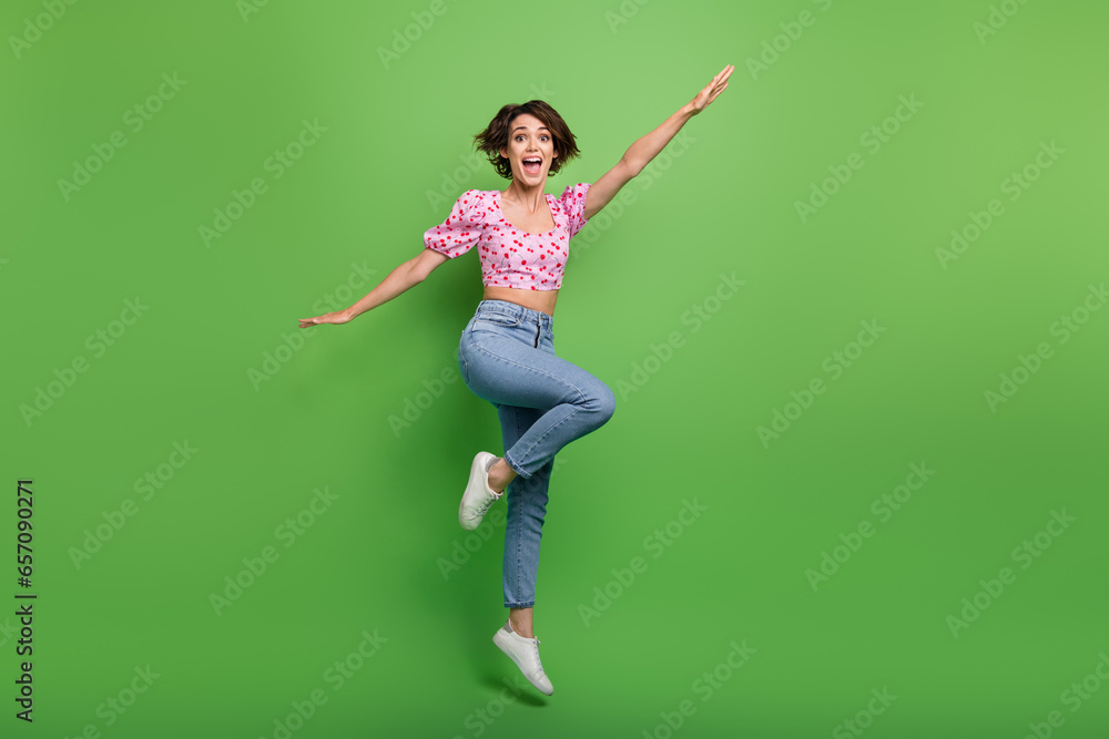 Full size photo of pretty young girl jumping run activity dressed stylish pink cherry print outfit isolated on green color background